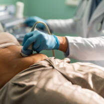 Gynecologist in sterile gloves using ultrasound scanner while examining female patient.